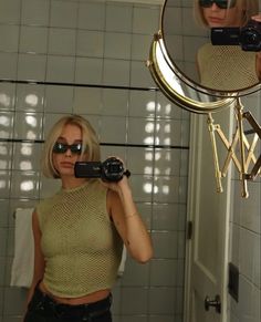 a woman taking a selfie in front of a mirror with her camera and sunglasses on