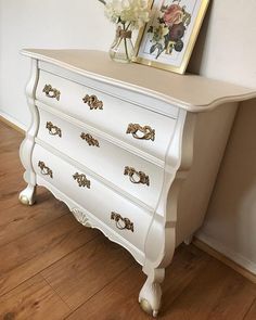 a white dresser sitting on top of a hard wood floor next to a framed painting