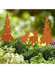 three wooden reindeer standing next to each other on top of green moss covered ground with trees and flowers in the background