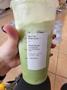 a person holding up a green smoothie in a plastic cup with a label on it