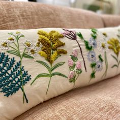 a close up of a pillow on a couch with flowers and leaves embroidered on it