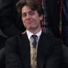 a man wearing a suit and tie sitting next to other people