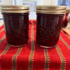 two jars of jam sitting on top of a red table cloth