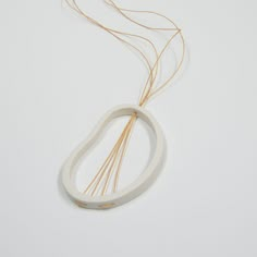 a white necklace with gold colored thread and two strands on the end, sitting on a white surface