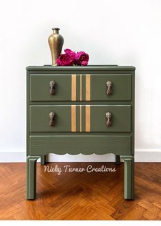 a green dresser with gold stripes on the drawers and pink flowers sitting on top of it