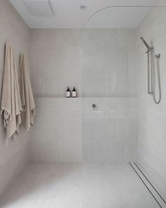 a white tiled bathroom with towels hanging on the wall and shower head in the corner