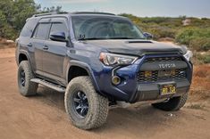 the front end of a blue toyota 4runner on a dirt road