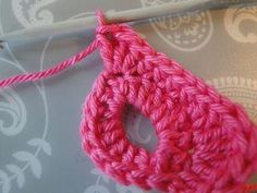 a pink crochet piece is being worked on by a knitting needle and thread