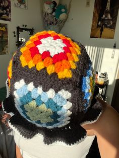 a person wearing a crocheted hat with multicolored circles on the top