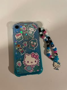 an iphone case with hello kitty on it and beads around the phone cover is sitting on a table