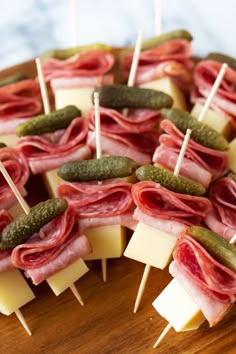 many different types of food on sticks with cheese and pickles attached to them, sitting on a wooden platter