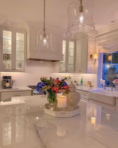 a large kitchen with white cabinets and marble counter tops is lit by candle lights that are hanging from the ceiling