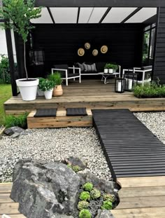 an outdoor patio with wooden steps and plants on the deck, surrounded by large rocks