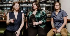 three women sitting at a bar with drinks