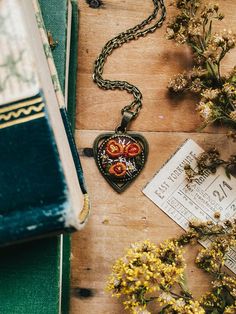 an open book and some flowers on a wooden table next to a necklace with two hearts