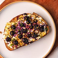 a white plate topped with a piece of bread covered in blueberries and other toppings