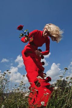 a woman in a long red dress is posing for the camera and holding a rose