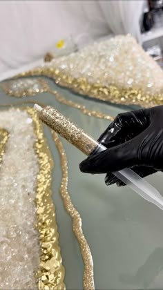 a pair of black gloves is being used to paint gold sequins on a glass surface