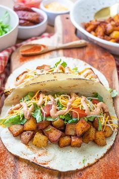 a tortilla filled with meat, lettuce and cheese on a wooden cutting board