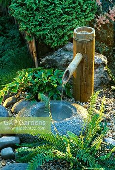 a water fountain in the middle of a garden with rocks and plants around it, surrounded by greenery