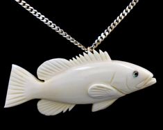 a white ceramic fish with green eyes on a silver chain and a black back ground