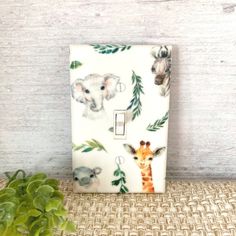 a white light switch cover with animals and leaves on it next to a potted plant