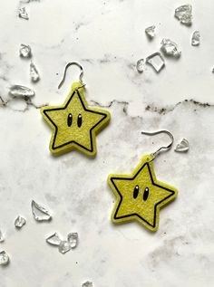 two yellow stars with faces on them are hanging from silver earwires against a marble background