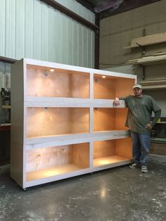 a man standing next to a tall white shelf filled with wooden shelves in a warehouse