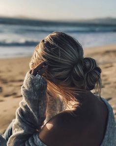 a woman sitting on the beach with her hair in a bun and texting instagram