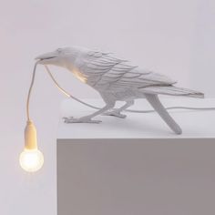 a white bird lamp sitting on top of a table next to a small light bulb