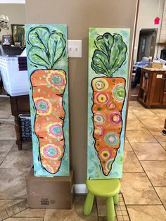 two paintings of carrots painted on canvases in a kitchen with tile flooring