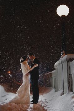 a bride and groom standing in the snow at night