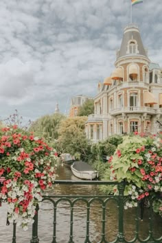 flowers are growing on the railing by the water in front of a building with a rainbow flag