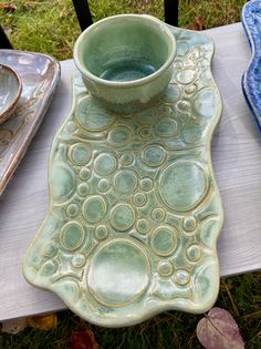 a green bowl sitting on top of a wooden table next to plates and bowls in the grass