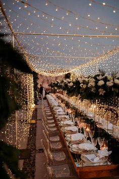 a long table is set with white plates and silverware for an outdoor dinner party