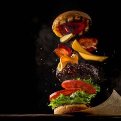 a hamburger with lettuce, tomato and pickles falling into the air on a black background