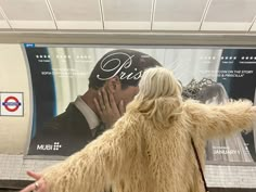 a man and woman are kissing in front of a poster on the wall at a subway station