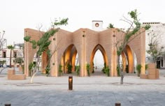 a building with arches and trees in front of it on a brick walkway surrounded by buildings