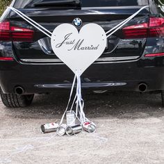 a black car parked in front of a white heart shaped sign that says just married