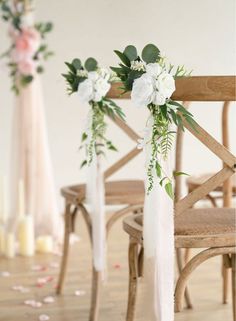 two wooden chairs with white flowers and greenery on the back one chair is empty