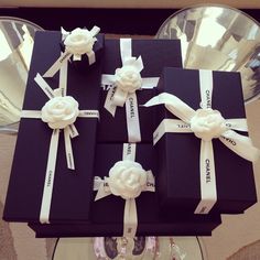 four black boxes with white ribbons and flowers on them are sitting on a glass table