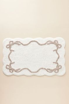 a white bath mat with gold trimmings on the edge and an oval shaped border