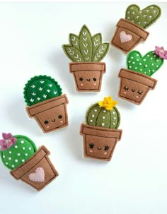 four felt cactus plant magnets with faces and hearts on them, sitting next to each other