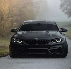 the front end of a black bmw car on a road with fog in the background