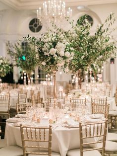 an elegant wedding reception with tall centerpieces and greenery in the center table