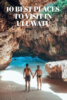 A young couple are standing side by side holding hands with their back to the camera as they look at waves coming in to the cave entrance of a very unique beach. The beach is inside the cave and the waves are seen crashing against the rocks ahead. The young couple are standing in matching black swim wear as they stand there. The cave is covered in greenery at the top and the light can be seen casting a shadow across the sand. Bali Beach Aesthetic, Bali Places To Visit, Bali Waterfalls, Things To Do In Bali, Uluwatu Bali