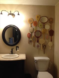 a bathroom with a toilet, mirror and various spoons on the wall above it