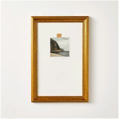 an empty gold frame hangs on the wall above a white framed photograph with a brown rectangle