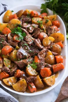 a white bowl filled with meat and potatoes on top of a marble table next to parsley