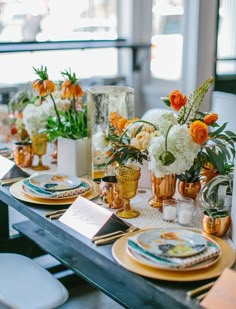 the table is set with gold and white plates, vases filled with orange flowers